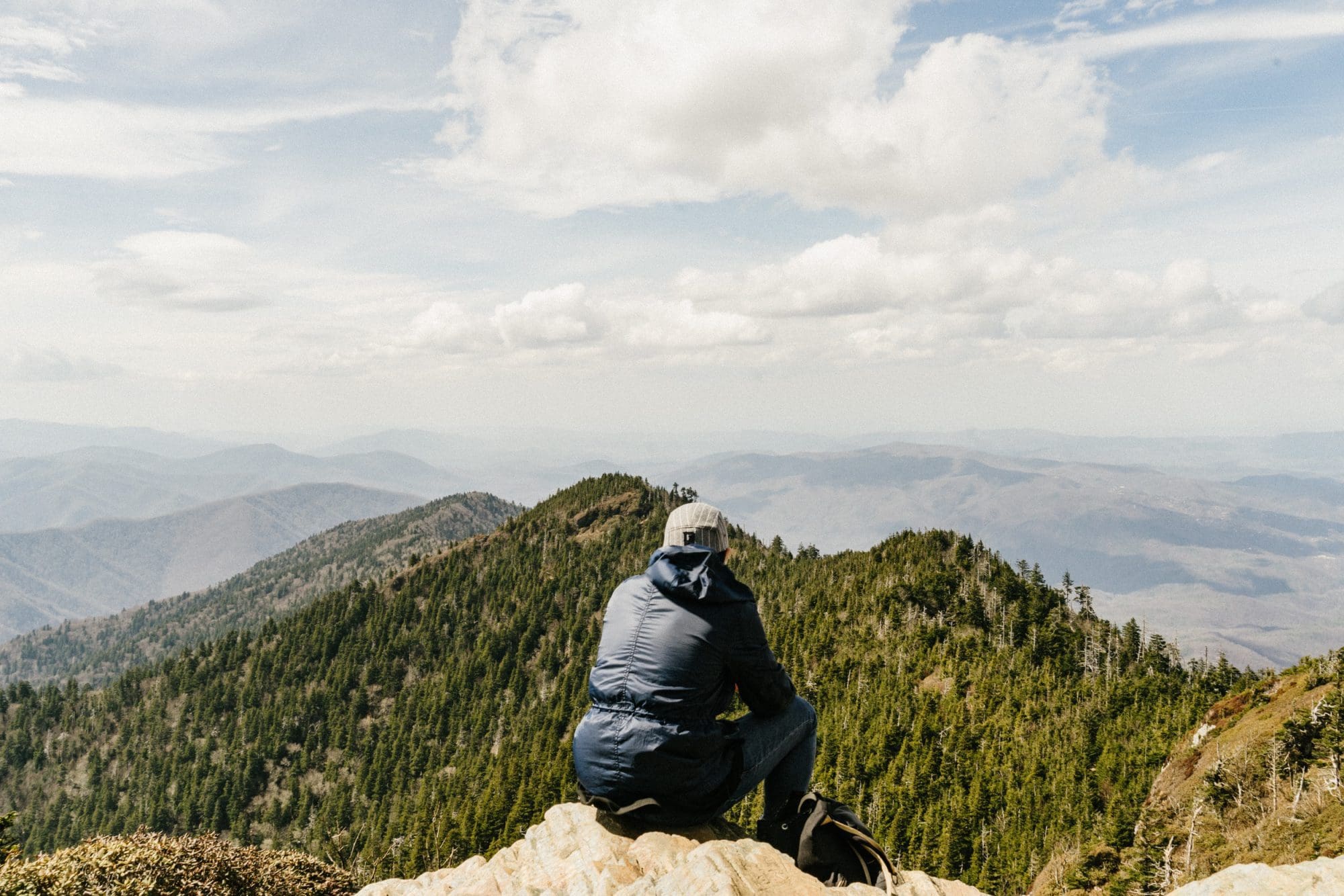 man sitting on top of a hill overlooking green mountains